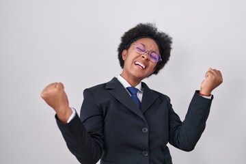 Poster - Beautiful african woman with curly hair wearing business jacket and glasses celebrating surprised and amazed for success with arms raised and eyes closed. winner concept.