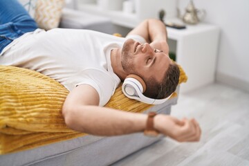 Sticker - Young caucasian man listening to music lying on sofa at home