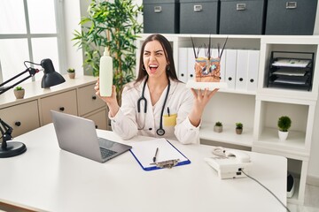 Poster - Hispanic doctor woman holding model of human anatomical skin and hair angry and mad screaming frustrated and furious, shouting with anger. rage and aggressive concept.