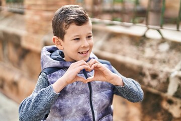 Wall Mural - Blond child smiling confident doing heart gesture with hands at street