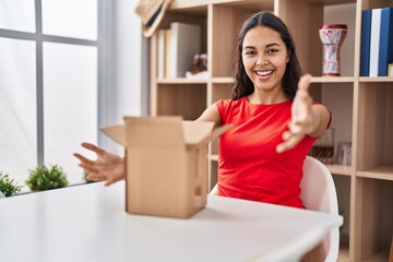 Sticker - Young brazilian woman looking inside cardboard box looking at the camera smiling with open arms for hug. cheerful expression embracing happiness.