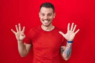 Poster - Young hispanic man standing over red background showing and pointing up with fingers number nine while smiling confident and happy.