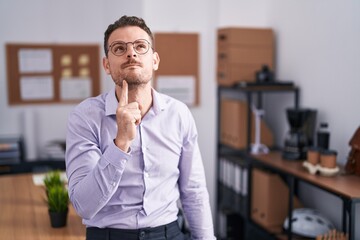 Canvas Print - Young hispanic man at the office thinking concentrated about doubt with finger on chin and looking up wondering