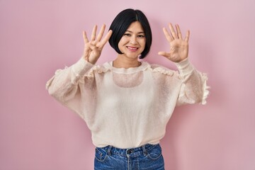 Sticker - Young asian woman standing over pink background showing and pointing up with fingers number nine while smiling confident and happy.