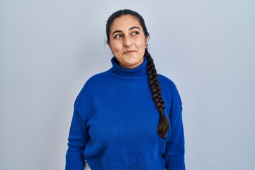 Sticker - Young hispanic woman standing over isolated background smiling looking to the side and staring away thinking.