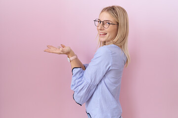 Wall Mural - Young caucasian business woman wearing id card pointing aside with hands open palms showing copy space, presenting advertisement smiling excited happy