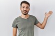 © Krakenimages.com - Young hispanic man with beard wearing casual t shirt over white background smiling cheerful presenting and pointing with palm of hand looking at the camera.