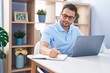 © Krakenimages.com - Young man using laptop writing on notebook at home