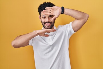 Sticker - Arab man standing over yellow background smiling cheerful playing peek a boo with hands showing face. surprised and exited