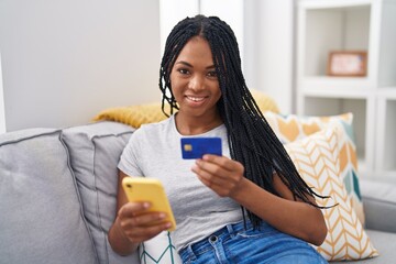 Poster - African american woman using smartphone and credit card sitting on sofa at home