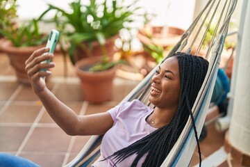 Wall Mural - African american woman make selfie by smartphone lying on hammock at home terrace