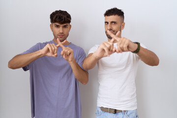 Canvas Print - Homosexual gay couple standing over white background rejection expression crossing fingers doing negative sign