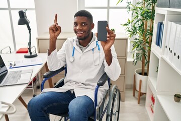 Poster - African american doctor man sitting on wheelchair holding smartphone surprised with an idea or question pointing finger with happy face, number one