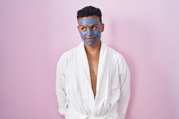 Sticker - Young hispanic man wearing beauty face mask and bath robe smiling looking to the side and staring away thinking.