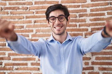 Poster - Young hispanic man standing over brick wall background pointing to you and the camera with fingers, smiling positive and cheerful