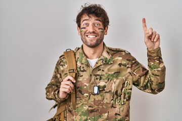 Poster - Hispanic young man wearing camouflage army uniform pointing finger up with successful idea. exited and happy. number one.