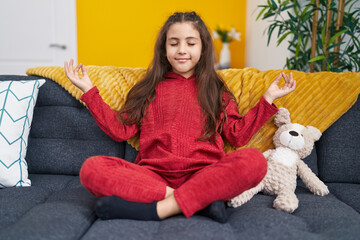 Sticker - Adorable hispanic girl doing yoga exercise sitting on sofa at home