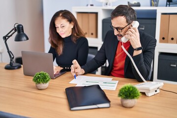 Sticker - Middle age man and woman business workers using laptop talking on the telephone at office