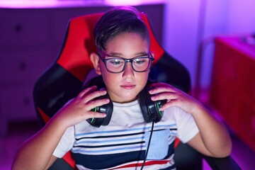 Sticker - Adorable hispanic boy streamer sitting on table with serious expression at gaming room