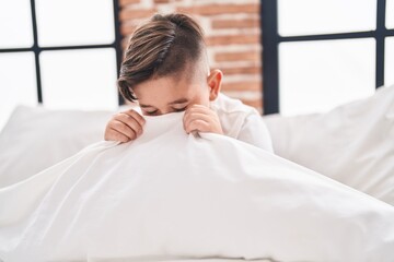 Sticker - Adorable hispanic boy sitting on bed covering face with bedsheet at bedroom