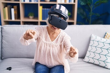 Sticker - Middle age grey-haired woman playing motorbike video game using virtual reality glasses at home