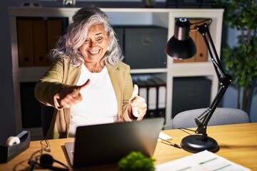 Sticker - Middle age woman with grey hair working using computer laptop late at night approving doing positive gesture with hand, thumbs up smiling and happy for success. winner gesture.