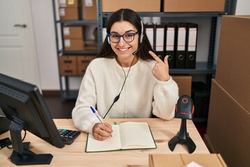 Canvas Print - Young hispanic woman working at small business ecommerce wearing headset smiling happy pointing with hand and finger