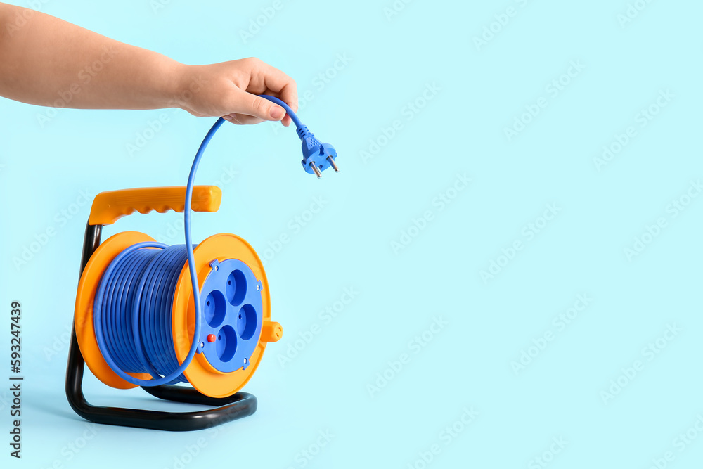 Female hand with extension electric cable reel on color background