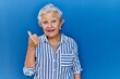 © Krakenimages.com - Senior woman with grey hair standing over blue background doing happy thumbs up gesture with hand. approving expression looking at the camera showing success.