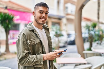 Wall Mural - Young hispanic man smiling confident using smartphone at street