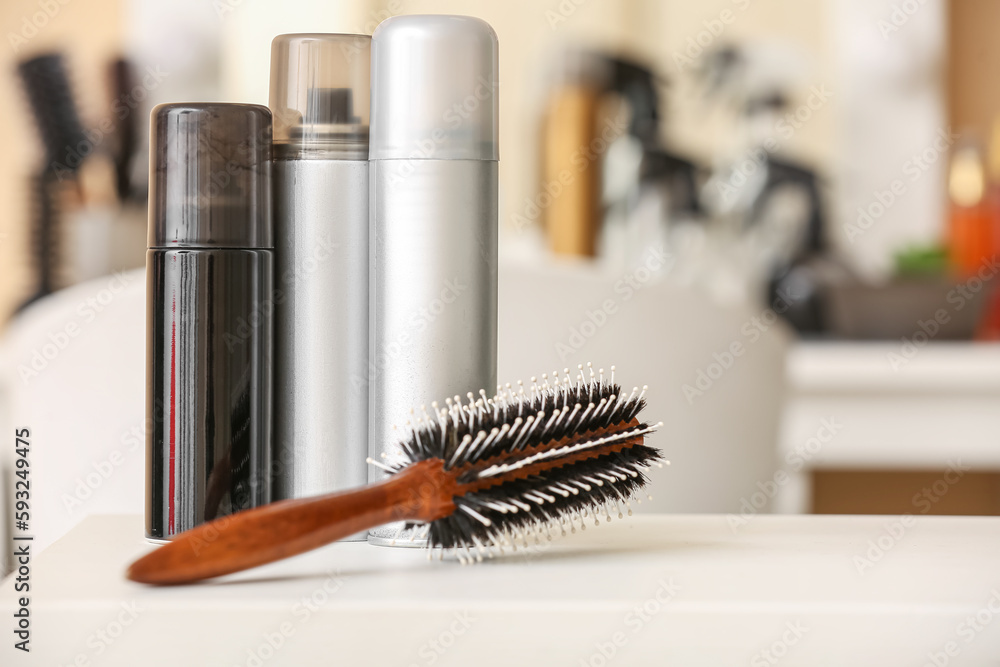 Different hair sprays and brush on table in beauty salon