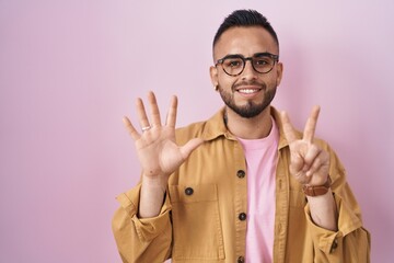 Wall Mural - Young hispanic man standing over pink background showing and pointing up with fingers number seven while smiling confident and happy.