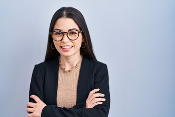 Poster - Young brunette woman standing over blue background happy face smiling with crossed arms looking at the camera. positive person.