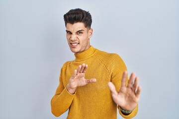 Canvas Print - Young hispanic man standing over blue background disgusted expression, displeased and fearful doing disgust face because aversion reaction.