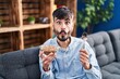 Young hispanic man with beard eating healthy whole grain cereals making fish face with mouth and squinting eyes, crazy and comical.