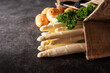 Fresh white asparagus and raw potatos in a shopping bag. Seasonal spring vegetables on modern black slate. Sunny kitchen scene for a healthy gastronomy concept with space for text.