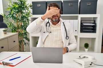 Canvas Print - Handsome middle age doctor man working at the clinic covering eyes with hand, looking serious and sad. sightless, hiding and rejection concept