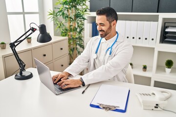 Canvas Print - Young hispanic man wearing doctor uniform using laptop working at clinic