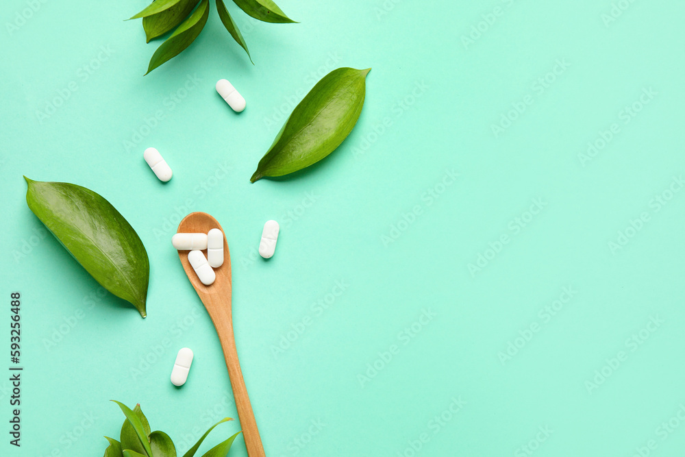 Spoon with pills and plant leaves on mint background