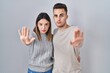 © Krakenimages.com - Young hispanic couple standing over white background doing stop sing with palm of the hand. warning expression with negative and serious gesture on the face.