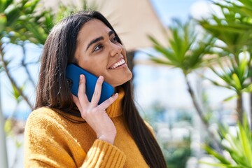 Wall Mural - Young hispanic woman smiling confident talking on the smartphone at park