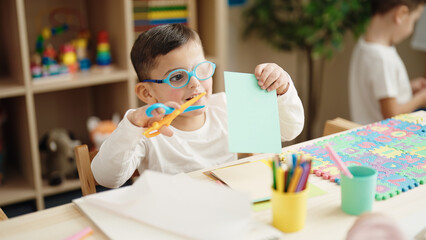 Sticker - Adorable hispanic boy student smiling confident cutting paper at kindergarten