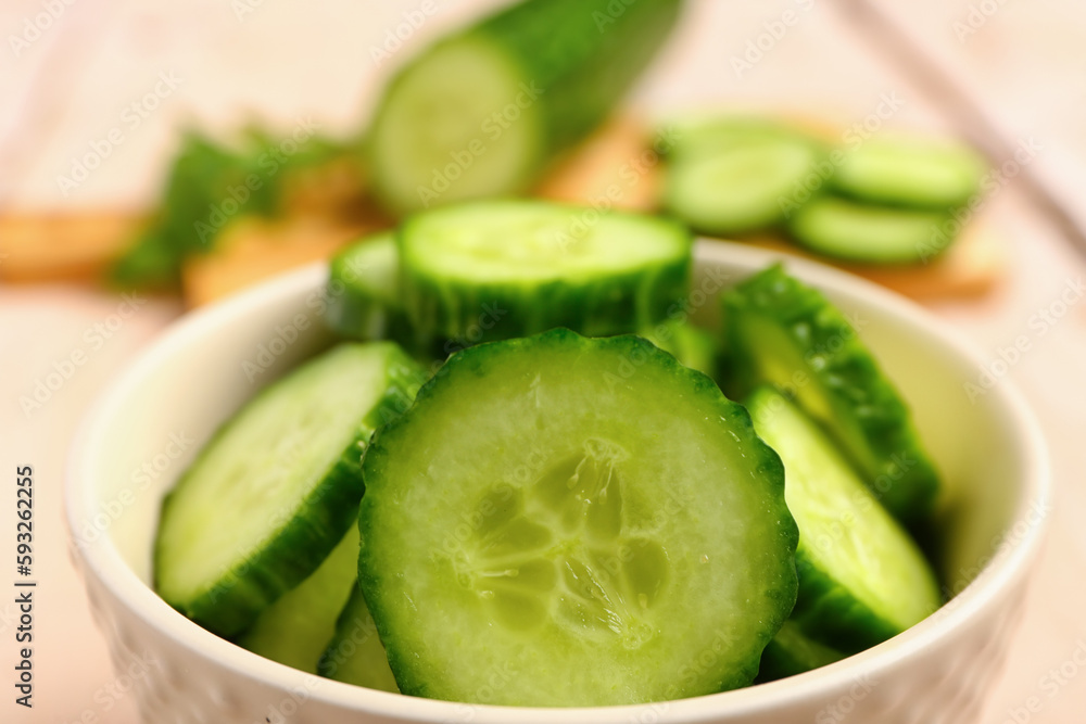 Bowl with fresh cut cucumber on light wooden background, closeup