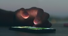 Finger of man touching scroll page app on mobile phone at night. Hands of person scrolling up photos of instagram on mobile phone, close up