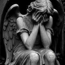 Grayscale Shot Of A Sculpture Of An Angel Weeping With A Blurry Background