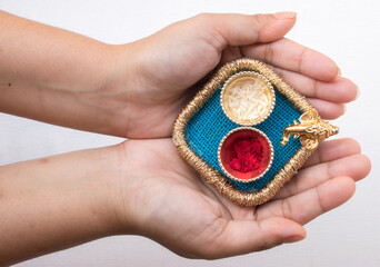 Hand holding beautiful small thali having God Ganesh face and red roli and chawal means tika and rice in white background. It is used for any hindu festival like Rakshbandhan, diwali, durga puja.