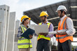 © Supachai - Team of construction engineers wearing vest and helmet safety discussing project at construction site. Group Indian foreman with laptop, paperwork working at factory making precast concrete wall.