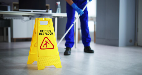 male janitor cleaning floor with caution wet floor sign