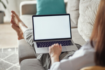 Wall Mural - Mockup white screen laptop woman using computer lying on sofa at home, back view, focus on screen