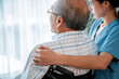 Rear view of a caregiver and her contented senior patient gazing out through the window. Elderly illness, nursing homes for the elderly, and pensioner life